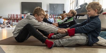 Børn laver yoga og sidder overfor hinanden og med hinanden i hænderne og laver strækøvelser. Foto: Frederikssund Kommune, Kenneth Jensen.