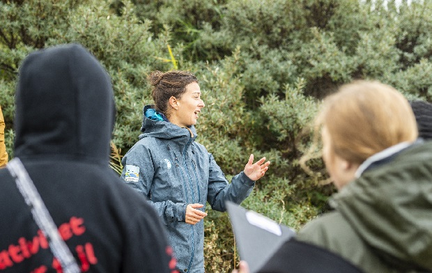 Kvinde står i naturen og fortæller noget, mens en gruppe unge lytter. Foto: Frederikssund Kommune, Kenneth Jensen.