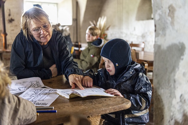 Kælderkøkkenet på Selsø Slot, hvor en kvinde og en dreng sidder ved et bord og kigger i en bog. Foto: Frederikssund Kommune, Kenneth Jensen.