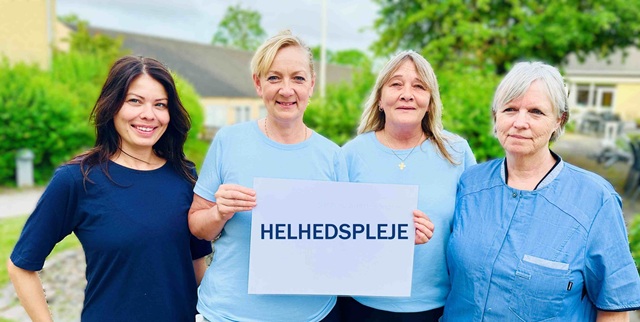 Fire kvindelige medarbejdere fra Døgnplejen i blåt tøj. De holder et skilt med ordet Helhedspleje. Foto: Irene Scharbau.
