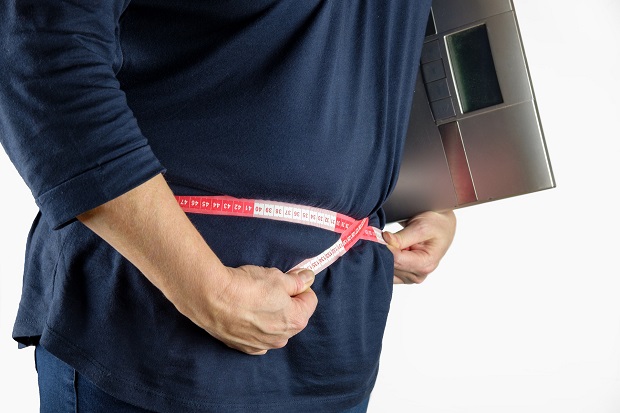 Person måler sin mave med et målebånd og har en badevægt under armen. Foto: Pixabay.