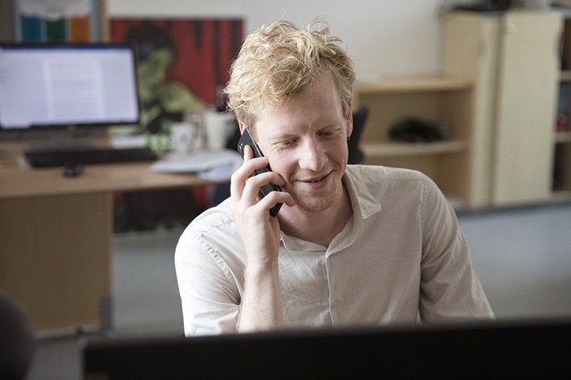 En glad medarbejder snakker i telefon ved sit skriveborg. Foto: Sofia Busk