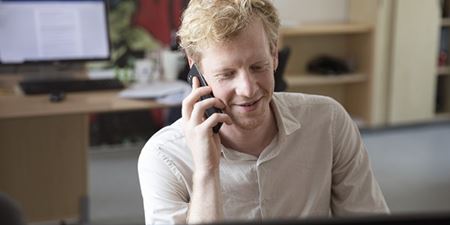 En glad medarbejder snakker i telefon ved sit skriveborg. Foto: Sofia Busk