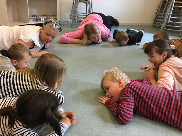 En gruppe børn og to voksne ligger i rundkreds på gulvet. Foto: Frederikssund Kommune.