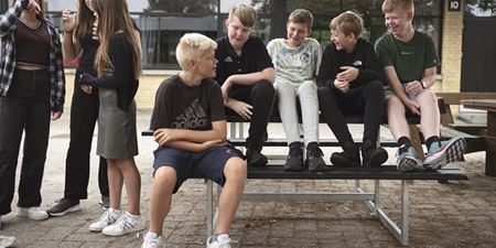 Børn og unge sidder på en bænk og snakker. Foto: Frederikssund Kommune.