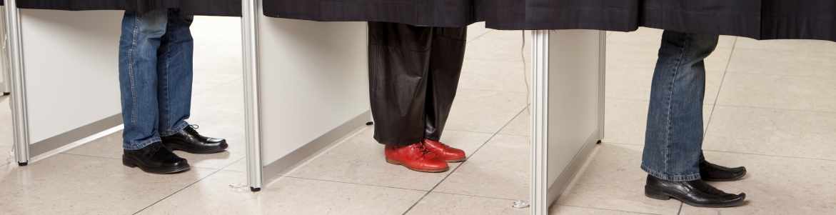 Tre stemmebokse på række. Under forhænget ses vælgernes fødder. Foto: Colourbox.