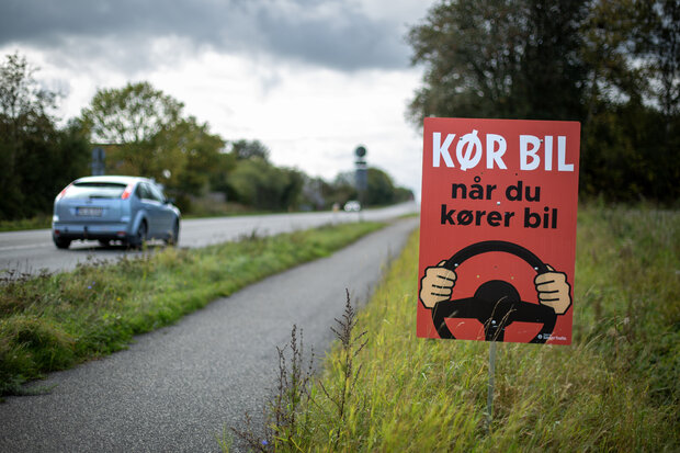Plakat med kampagnebudskab langs en befærdet landevej. Foto: Rådet for Sikker Trafik.