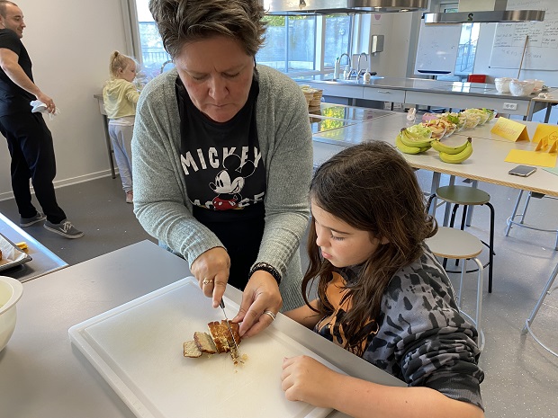 Lærer Rikke Herlev viser en elev, hvordan man skærer fiskefrikadeller ud til madpakken. Foto: Frederikssund Kommune.