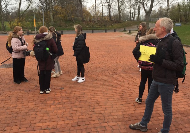 Lærer står med gult nummerskilt og eleverne samles med afstand foran læreren. Foto: Frederikssund Kommune.