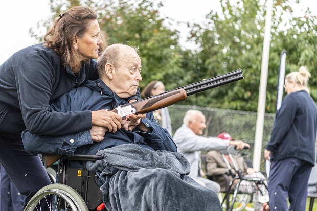 Ældre herre i kørestol og med lasergevær får hjælp af kvindelig medarbejder fra omsorgscentret. Foto: Frederikssund Kommune, Kenneth Jensen.