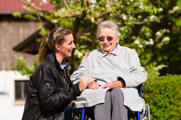 Ældre kvinde i kørestol - ung kvinde støtter hende omsorgsfuldt. Foto: Colourbox.