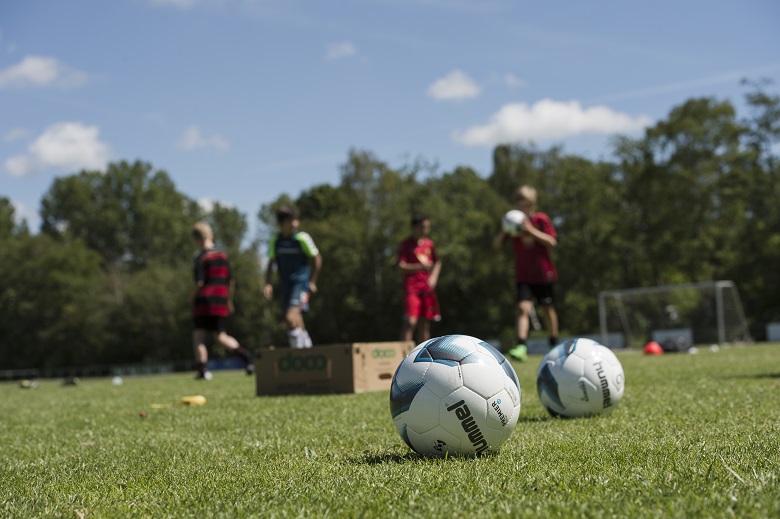 Fodbolde på græsplæne og fodboldspillere i baggrunden. Foto: Frederikssund Kommune, Kenneth Jensen.