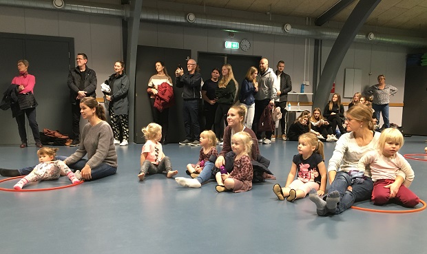 Voksne og børn sidder på gulvet i gymnastiksal og lytter. Foto: Frederikssund Kommune.