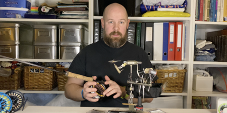 Mand ved arbejdsbord med grej til fluebinding. Foto: Fishing Zealand.