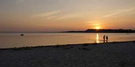 To mennesker går i strandkanten i solnedgangen. Foto: Frederikssund Kommune, Kenneth Jensen.
