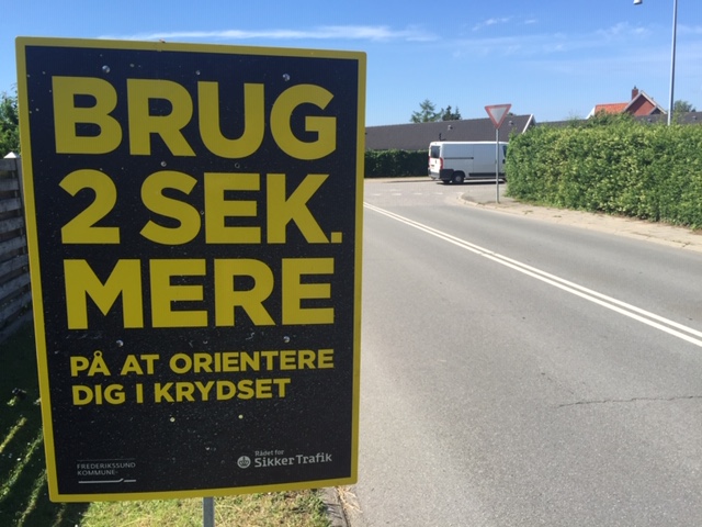 Skilt i vejsiden opfordrer til at bruge 2 sek. mere på at orientere sig i krydset. Foto: Frederikssund Kommune.