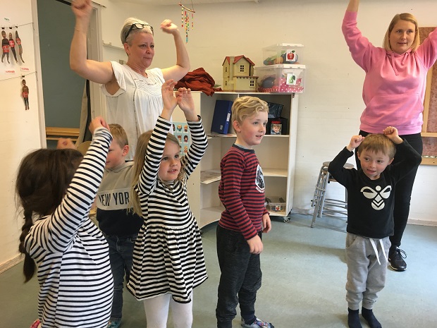 Fem børn og to voksne står med armene over hovederne. Foto: Frederikssund Kommune.