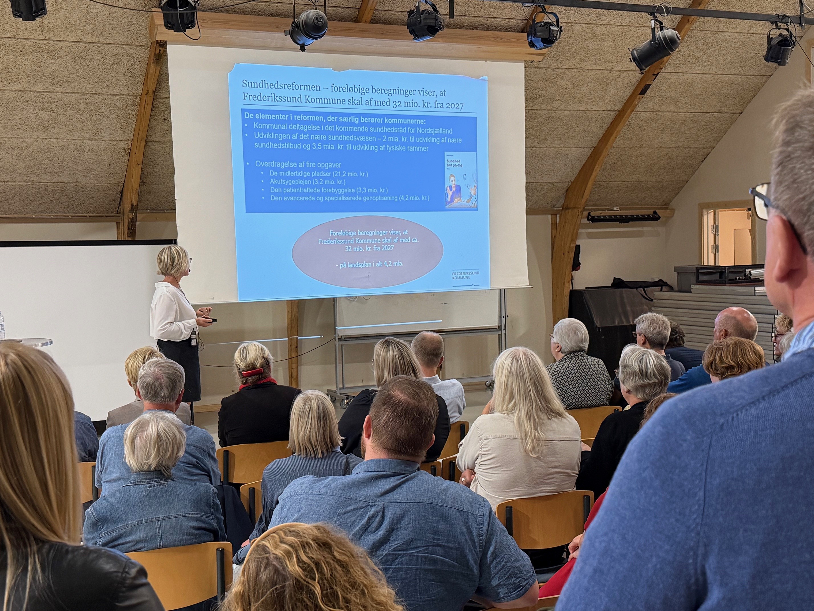 Der holdes oplæg om Budget 2026, mens tilhørerne sidder i rækker. Foto: Frederikssund Kommune