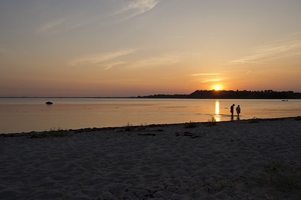 Par går ved strand med solnedgang i baggrunden. Foto: Frederikssund Kommune, Kenneth Jensen.