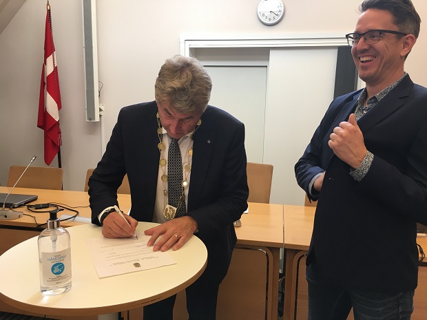 Borgmesteren skriver under på papirerne mens Andrew John Krant er klar til håndtryk. Foto: Frederikssund Kommune.